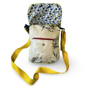 Sac bandoulière ouvert avec doublure à motifs géométriques colorés, poche extérieure zippée sur tissu beige à motifs végétaux noirs